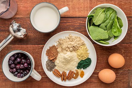 ingredients of healthy breakfast smoothie: almond milk, raw eggs, fresh spinach, frozen blueberries, whey protein, cacao, chiai seeds, pecan nuts, maca root powder, spirulina,  spices (cinnamon, ginger, turmeric) with a stick blender on a rustic table Stock Photo - Budget Royalty-Free & Subscription, Code: 400-07794858