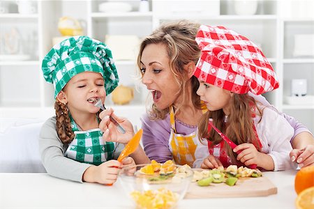 Woman and little girls preparing a fruit salad, tasting the ingredients - happy family moments Photographie de stock - Aubaine LD & Abonnement, Code: 400-07793735