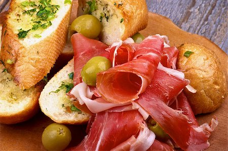 pane all'aglio - Heap of Delicious Tapas with Smoked Jamon, Garlic Bread and Green Olives closeup on Wooden Plate Fotografie stock - Microstock e Abbonamento, Codice: 400-07818317