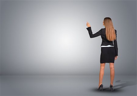 suit shoes back - Businesswoman in suit standing in an empty gray room and pointing finger at wall. Rear view Stock Photo - Budget Royalty-Free & Subscription, Code: 400-07826266