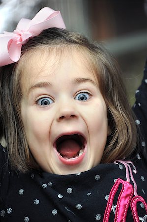 Little girl screams for joy in a closeup photo.  She is wearing a pink hairbow and black polka dotted shirt.  Her mouth is wide open and her eyes sparkle. Foto de stock - Royalty-Free Super Valor e Assinatura, Número: 400-07829418