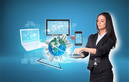 simsearch:400-07821752,k - Beautiful businesswomen in suit using digital tablet. Earth with buildings and laptop, tablets and smartphone. Element of this image furnished by NASA Foto de stock - Royalty-Free Super Valor e Assinatura, Número: 400-07821691