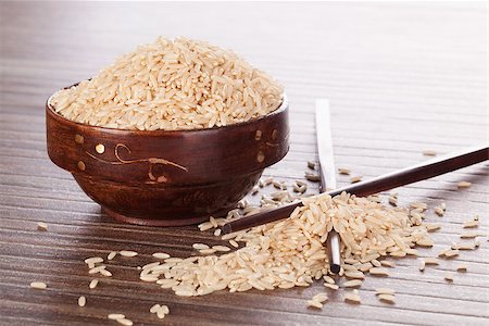 Natural brown rice background. Raw uncooked rice in wooden bowl with chopsticks on brown background. Culinary rice eating. Foto de stock - Super Valor sin royalties y Suscripción, Código: 400-07822925