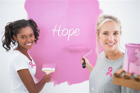 simsearch:400-07834992,k - Smiling housemates painting wall pink against pink breast cancer awareness ribbon Fotografie stock - Microstock e Abbonamento, Codice: 400-07834987