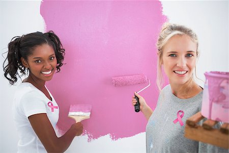 simsearch:400-07834992,k - Smiling housemates painting wall pink against pink breast cancer awareness ribbon Fotografie stock - Microstock e Abbonamento, Codice: 400-07834980