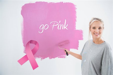 simsearch:400-07834992,k - Happy young woman painting her wall pink against pink breast cancer awareness ribbon Fotografie stock - Microstock e Abbonamento, Codice: 400-07834981