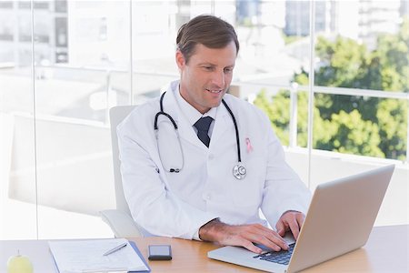 doctor wearing stethoscope - Happy doctor working on a laptop wearing breast cancer awareness ribbon Stock Photo - Budget Royalty-Free & Subscription, Code: 400-07835151