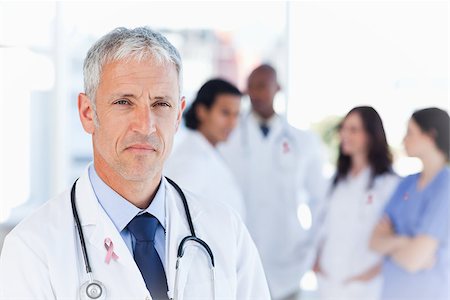 Mature doctor looking straight ahead wearing breast cancer awareness ribbon Foto de stock - Super Valor sin royalties y Suscripción, Código: 400-07835163