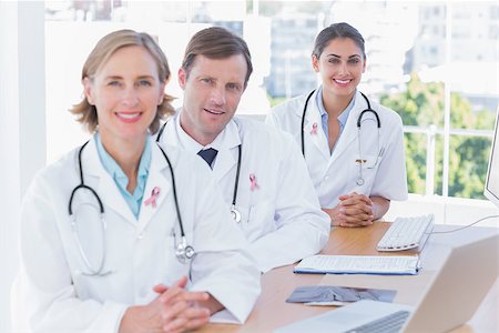 Smiling doctors posing at their desk wearing breast cancer awareness ribbon Photographie de stock - Aubaine LD & Abonnement, Code: 400-07835182