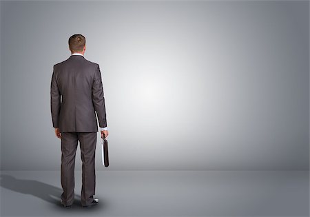 Businessman in suit standing in an empty gray room. Rear view. In hand holding briefcase Stock Photo - Budget Royalty-Free & Subscription, Code: 400-07894682