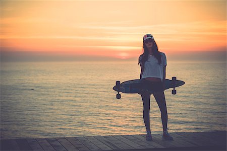 Beautiful and fashion young woman posing at teh sunset with a skateboard - File a little bit noisy Stock Photo - Budget Royalty-Free & Subscription, Code: 400-07896638