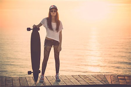 Beautiful and fashion young woman posing at teh sunset with a skateboard - File a little bit noisy Stock Photo - Budget Royalty-Free & Subscription, Code: 400-07896632