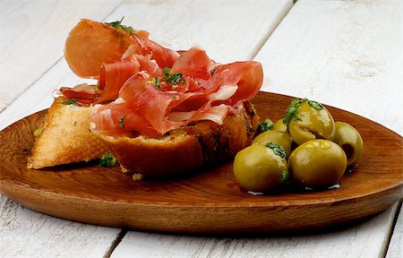 pane all'aglio - Delicious Tapas with Smoked Jamon, Garlic Bread and Heap of Green Olives on Wooden Plate closeup on White Wooden background Fotografie stock - Microstock e Abbonamento, Codice: 400-07899226