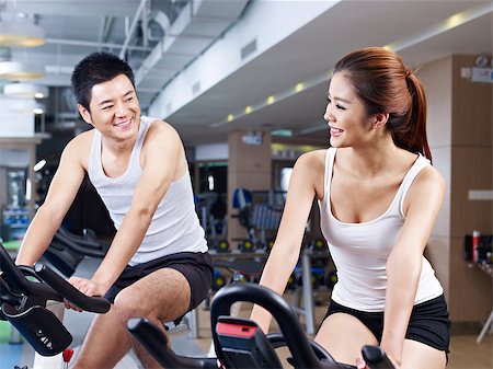 fitness asian couple - young man and woman talking while exercising on bicycle in fitness center. Foto de stock - Super Valor sin royalties y Suscripción, Código: 400-07892685