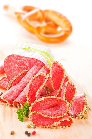 simsearch:400-06852716,k - Salami slices on wooden board with fresh herbs and pepper corns. Pastry in background. Stockbilder - Microstock & Abonnement, Bildnummer: 400-07893661