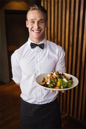 simsearch:400-05230474,k - Smiling waiter showing plate of salad to camera in a bar Stock Photo - Budget Royalty-Free & Subscription, Code: 400-07926558