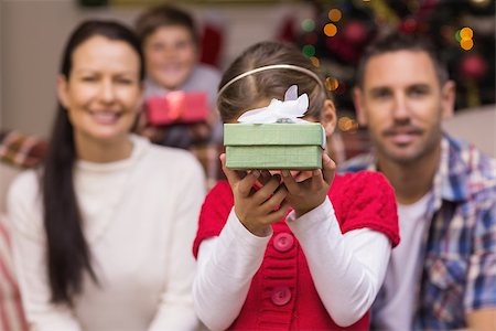 simsearch:400-06930138,k - Daughter showing a gift with her family behind at home in the living room Stock Photo - Budget Royalty-Free & Subscription, Code: 400-07928787