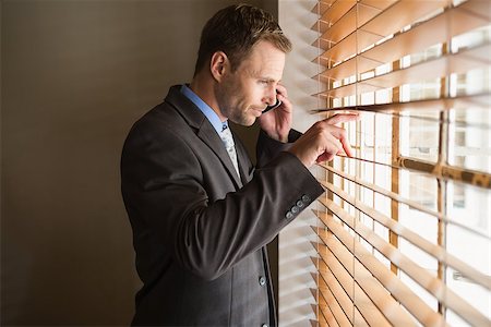 simsearch:400-07266908,k - Businessman peeking through blinds while on call in office Photographie de stock - Aubaine LD & Abonnement, Code: 400-07929738