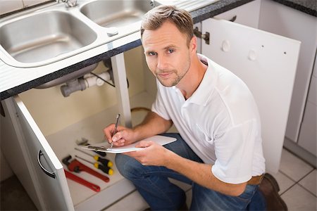 simsearch:400-07929795,k - Plumber crouching and taking notes in the kitchen Stock Photo - Budget Royalty-Free & Subscription, Code: 400-07929799