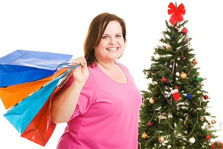 Happy plus sized model holding shopping bags, standing in front of a Christmas tree.  Isolated on white. Foto de stock - Super Valor sin royalties y Suscripción, Código: 400-07920878