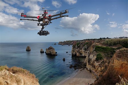 drone uav - A drone with raised landing gears and a camera flying in beautiful cloudy skies along spectacular sea cliffs with a calm ocean in the background Stock Photo - Budget Royalty-Free & Subscription, Code: 400-07923075