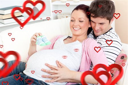 simsearch:400-06690931,k - Portrait of a happy pregnant woman holding baby shoes and of her husband on a sofa against hearts Fotografie stock - Microstock e Abbonamento, Codice: 400-07934648