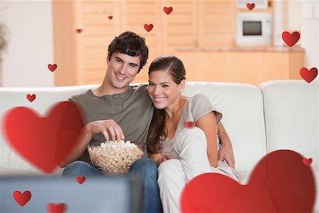 simsearch:400-05748048,k - Couple with popcorn on the sofa watching a movie against hearts Stockbilder - Microstock & Abonnement, Bildnummer: 400-07934728