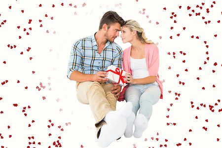 simsearch:400-07726694,k - Attractive young couple sitting holding a gift against red love hearts Foto de stock - Royalty-Free Super Valor e Assinatura, Número: 400-07935129