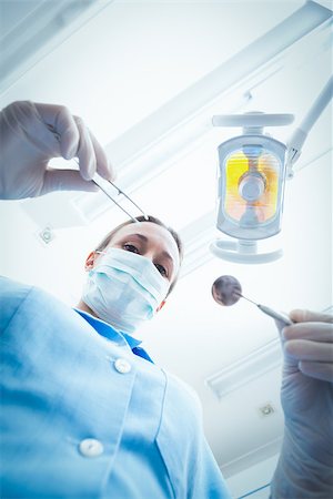 simsearch:400-07938947,k - Low angle portrait of female dentist in surgical mask holding dental tools Photographie de stock - Aubaine LD & Abonnement, Code: 400-07938955