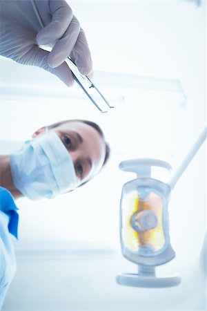 simsearch:400-07938947,k - Low angle portrait of female dentist in surgical mask holding dental tool Photographie de stock - Aubaine LD & Abonnement, Code: 400-07938951