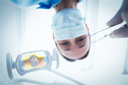 simsearch:400-07938947,k - Low angle portrait of female dentist in surgical mask holding dental tool Photographie de stock - Aubaine LD & Abonnement, Code: 400-07938952