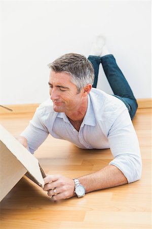 simsearch:400-07928013,k - Septic man lying on floor and looking inside the box at arpartment Fotografie stock - Microstock e Abbonamento, Codice: 400-07930720