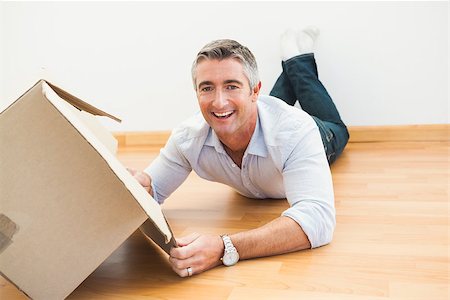 simsearch:400-07928013,k - Happy man lying on floor with box looking at camera at apartment Fotografie stock - Microstock e Abbonamento, Codice: 400-07930721