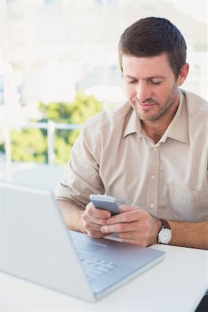 simsearch:400-07931035,k - Smiling casual businessman sending a text at his desk in his office Stock Photo - Budget Royalty-Free & Subscription, Code: 400-07931118