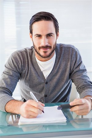 simsearch:400-07931035,k - Happy casual man writing on sheets paying bills in the office Stock Photo - Budget Royalty-Free & Subscription, Code: 400-07931312
