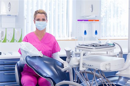 simsearch:400-07940798,k - Dentist in pink scrubs looking at camera beside chair at the dental clinic Stock Photo - Budget Royalty-Free & Subscription, Code: 400-07940777