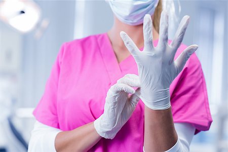simsearch:400-07941465,k - Dentist in pink scrubs putting on surgical gloves at the dental clinic Stock Photo - Budget Royalty-Free & Subscription, Code: 400-07940788