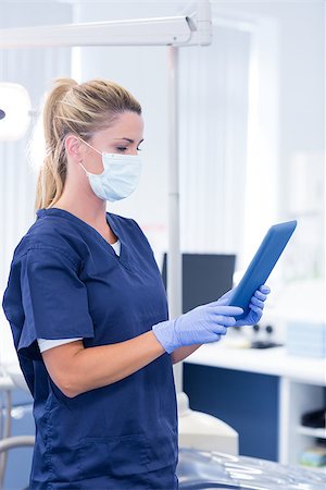 simsearch:400-07940798,k - Dentist in mask and blue scrubs using her tablet at the dental clinic Stock Photo - Budget Royalty-Free & Subscription, Code: 400-07940814