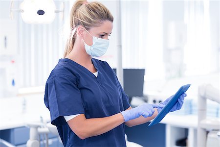 simsearch:400-07940798,k - Dentist in mask and blue scrubs using her tablet at the dental clinic Stock Photo - Budget Royalty-Free & Subscription, Code: 400-07940815