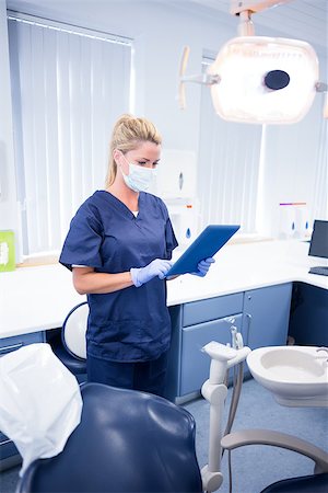 simsearch:400-07940798,k - Dentist in mask and blue scrubs using her tablet at the dental clinic Stock Photo - Budget Royalty-Free & Subscription, Code: 400-07940813