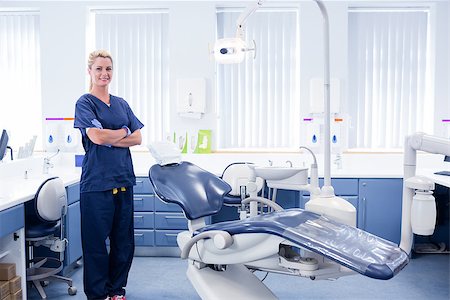 simsearch:400-07940798,k - Dentist in blue scrubs standing with arms crossed beside chair at the dental clinic Stock Photo - Budget Royalty-Free & Subscription, Code: 400-07940820
