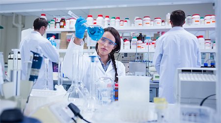 Chemist raising beaker of blue liquid with colleagues behind in busy lab Stock Photo - Budget Royalty-Free & Subscription, Code: 400-07941323