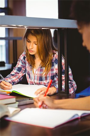 simsearch:400-07939821,k - Serious student sitting at desk writing in notepad in library Photographie de stock - Aubaine LD & Abonnement, Code: 400-07941711