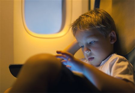 Close-up shot of a little boy playing on touch pad during in the plane. Child looking tired or bored Stock Photo - Budget Royalty-Free & Subscription, Code: 400-07955849