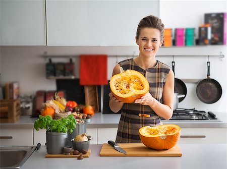 simsearch:400-07956836,k - Portrait of happy young housewife in kitchen showing pumpkin Foto de stock - Royalty-Free Super Valor e Assinatura, Número: 400-07956528