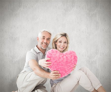 simsearch:400-07957430,k - Happy couple sitting and holding heart pillow against weathered surface Photographie de stock - Aubaine LD & Abonnement, Code: 400-07957435