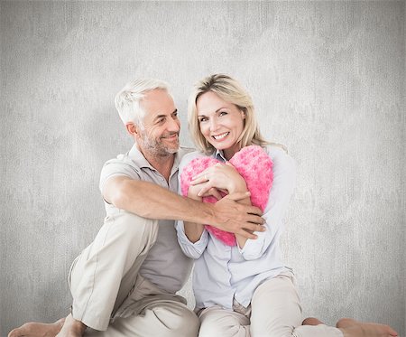 simsearch:400-07957430,k - Happy couple sitting and holding heart pillow against weathered surface Photographie de stock - Aubaine LD & Abonnement, Code: 400-07957436