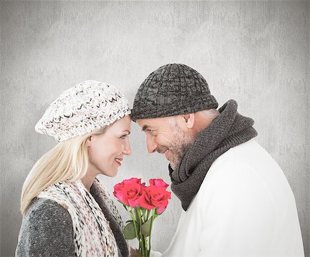 simsearch:400-07957339,k - Smiling couple in winter fashion posing with roses against weathered surface Photographie de stock - Aubaine LD & Abonnement, Code: 400-07957432