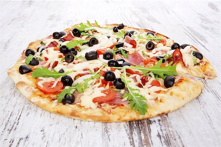 simsearch:400-04302812,k - Delicious pizza with ham, black olives, fresh herbs and melted cheese on white wooden background. Traditional rustic style pizza eating. Fotografie stock - Microstock e Abbonamento, Codice: 400-07952852