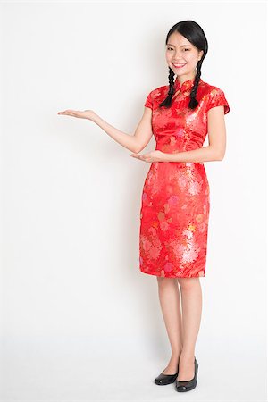 Portrait of full length Asian Chinese girl, hands showing something, in traditional red cheongsam standing on plain background. Stock Photo - Budget Royalty-Free & Subscription, Code: 400-07974004